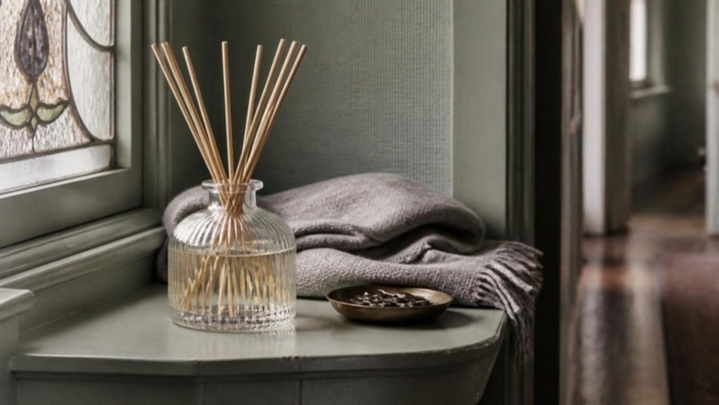 A ribbed glass reed diffuser on a painted hallway shelf beside a wool throw