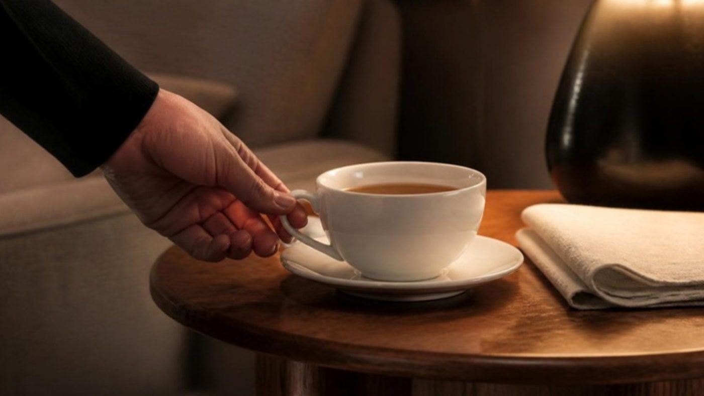 A hand setting down a cup of tea on a walnut side table
