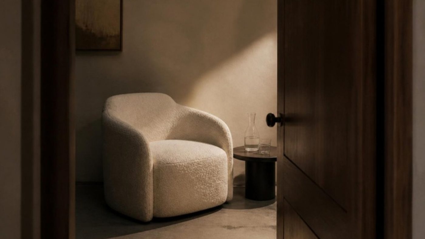 A quiet side room seen through a half-open walnut door, one armchair in lamp light